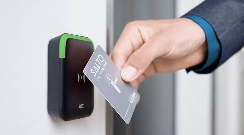 Person using a contactless card to unlock a black and green smart door lock mounted on a wall
