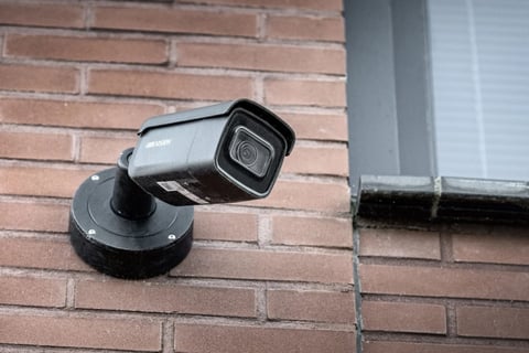 Black security camera mounted on red brick wall near window
