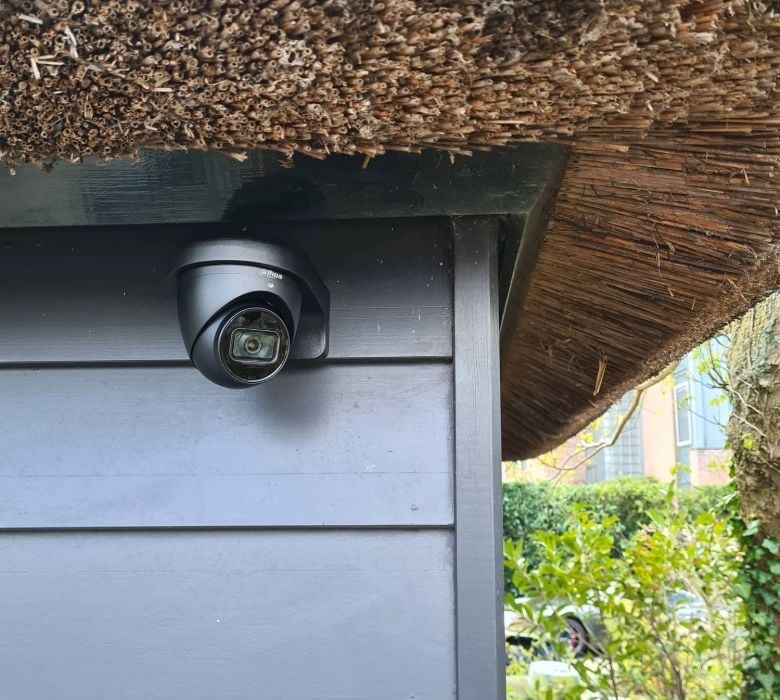 Security camera mounted on gray exterior wall under thatched roof overhang
