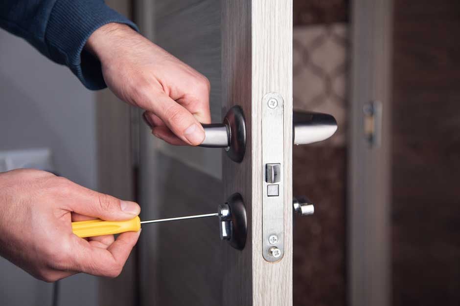 Hands adjusting a door lock mechanism with a screwdriver on a white door frame