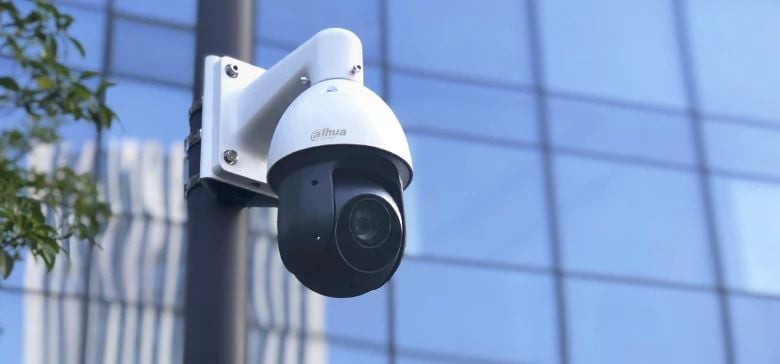 White and black PTZ security camera mounted on pole with blurred building in background