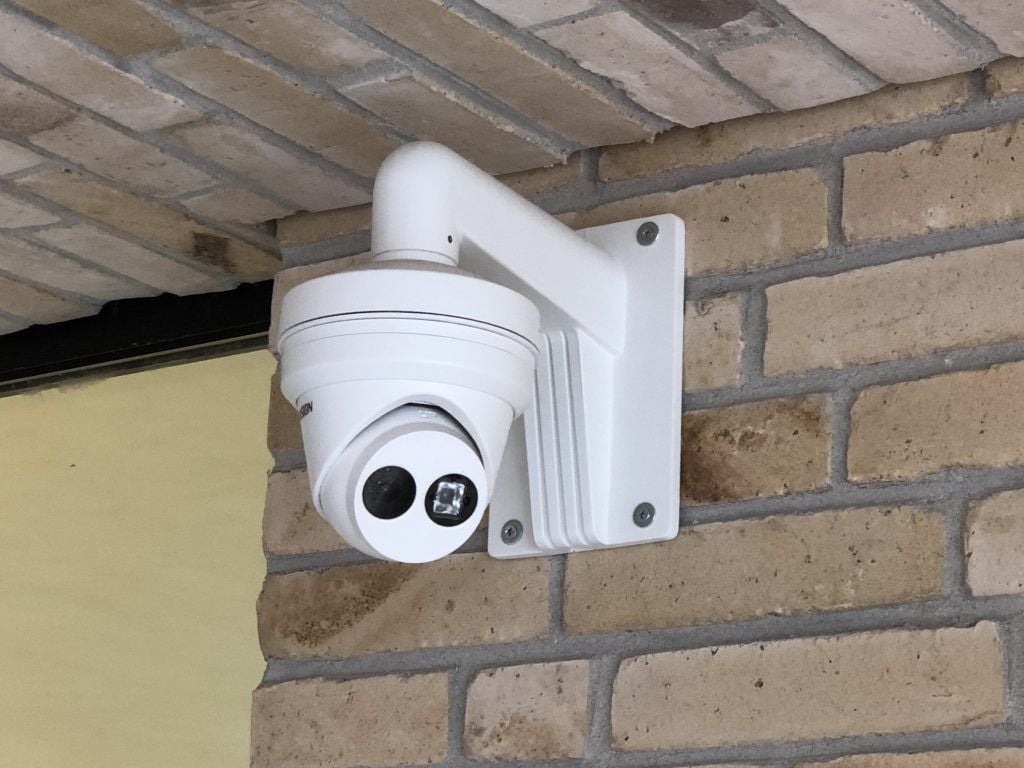 White dome security camera mounted on a brick wall under a soffit