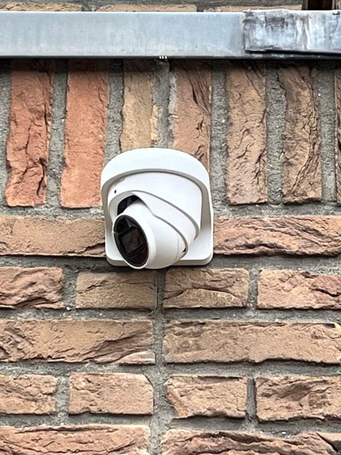 White dome security camera mounted on a brick wall with metal trim above