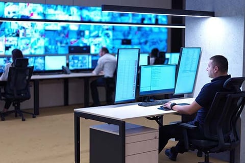 IT professionals working at computer stations in a modern control room with large blue monitoring displays on the wall